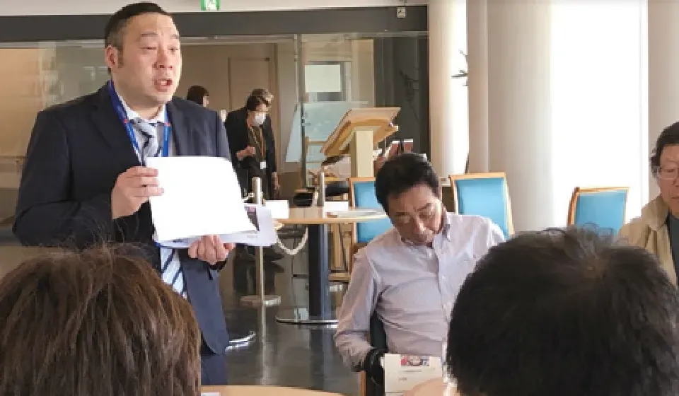 交流会で資料を手に参加者へ説明する JBTA スタッフの様子